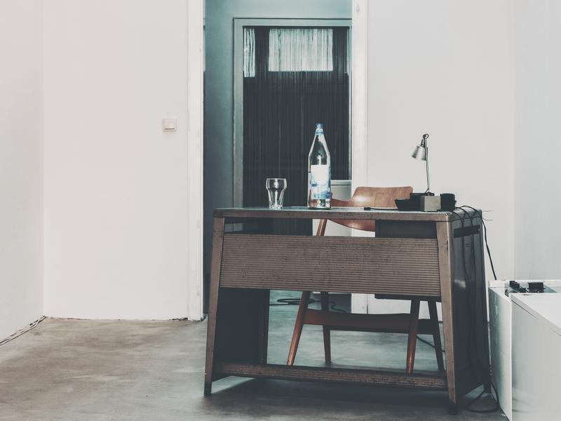 Photo d’illustration : un local aux murs blancs, avec un bureau en bois, une chaise et une bouteille d’eau.