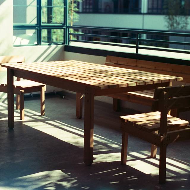 Photo d’illustration : une terrasse vitrée avec une longue table et des bancs en bois, au soleil.