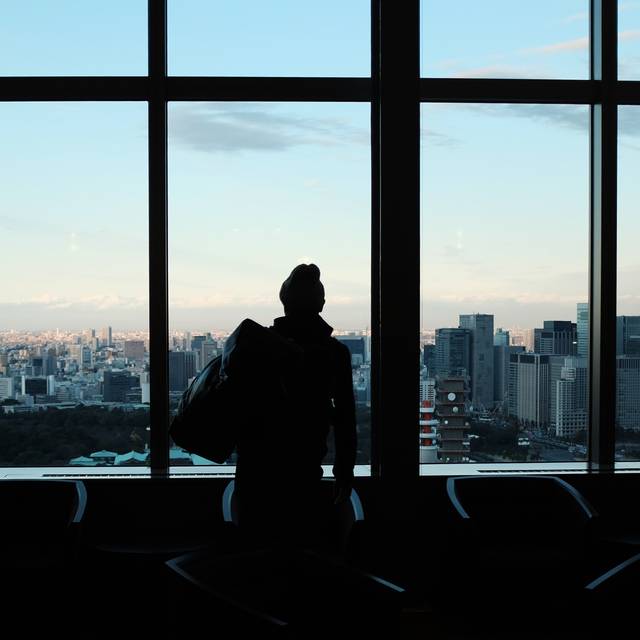 Photo d’illustration : une grande baie vitrée au crépuscule, avec la silhouette d’une personne devant la ville.