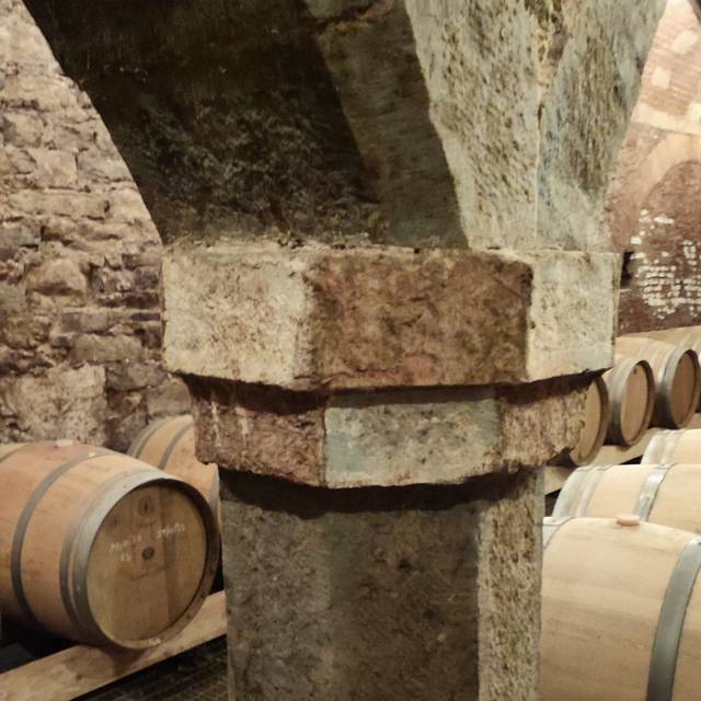 Photo d’illustration : un pilier en pierre dans une cave voûtée, avec des fûts en bois derrière.