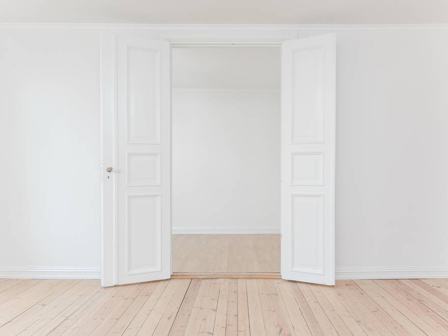 Photo d’illustration : une pièce vide au parquet clair, avec une porte à deux battants blanche ouverte sur la pièce suivante.